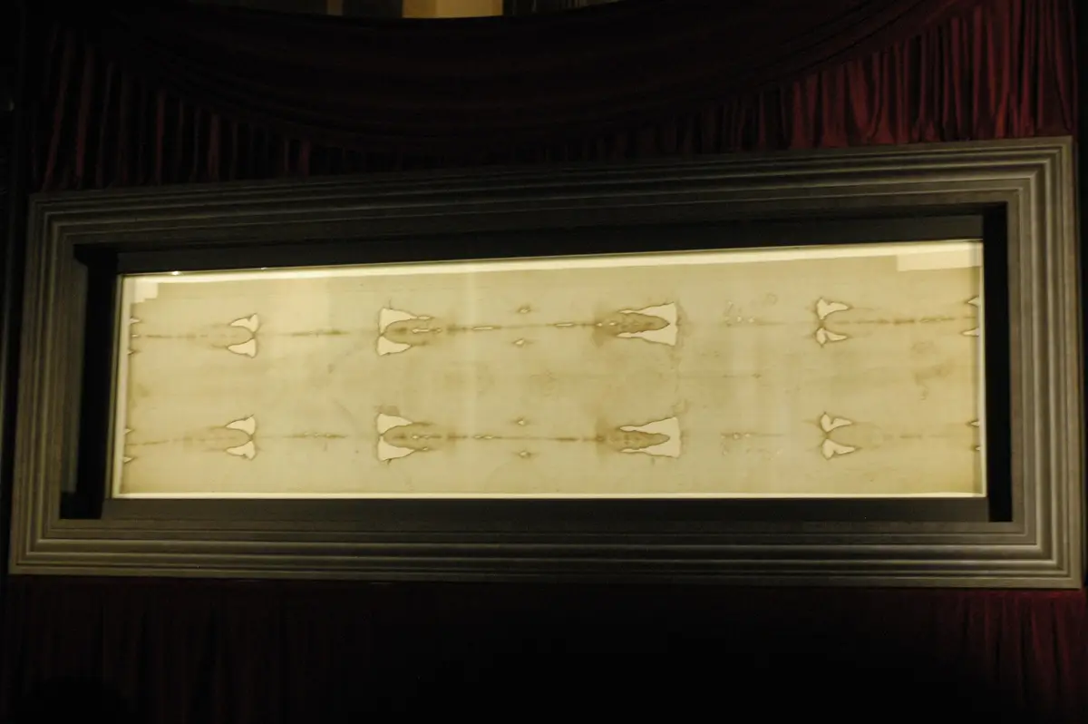 The Shroud displayed flat in a lit frame in the cathedral in 2010, with a crowd before it.
